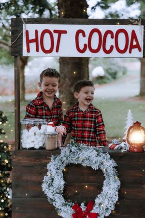 A festive hot cocoa stand decorated with white wreaths and Christmas lights creates a cozy winter scene.