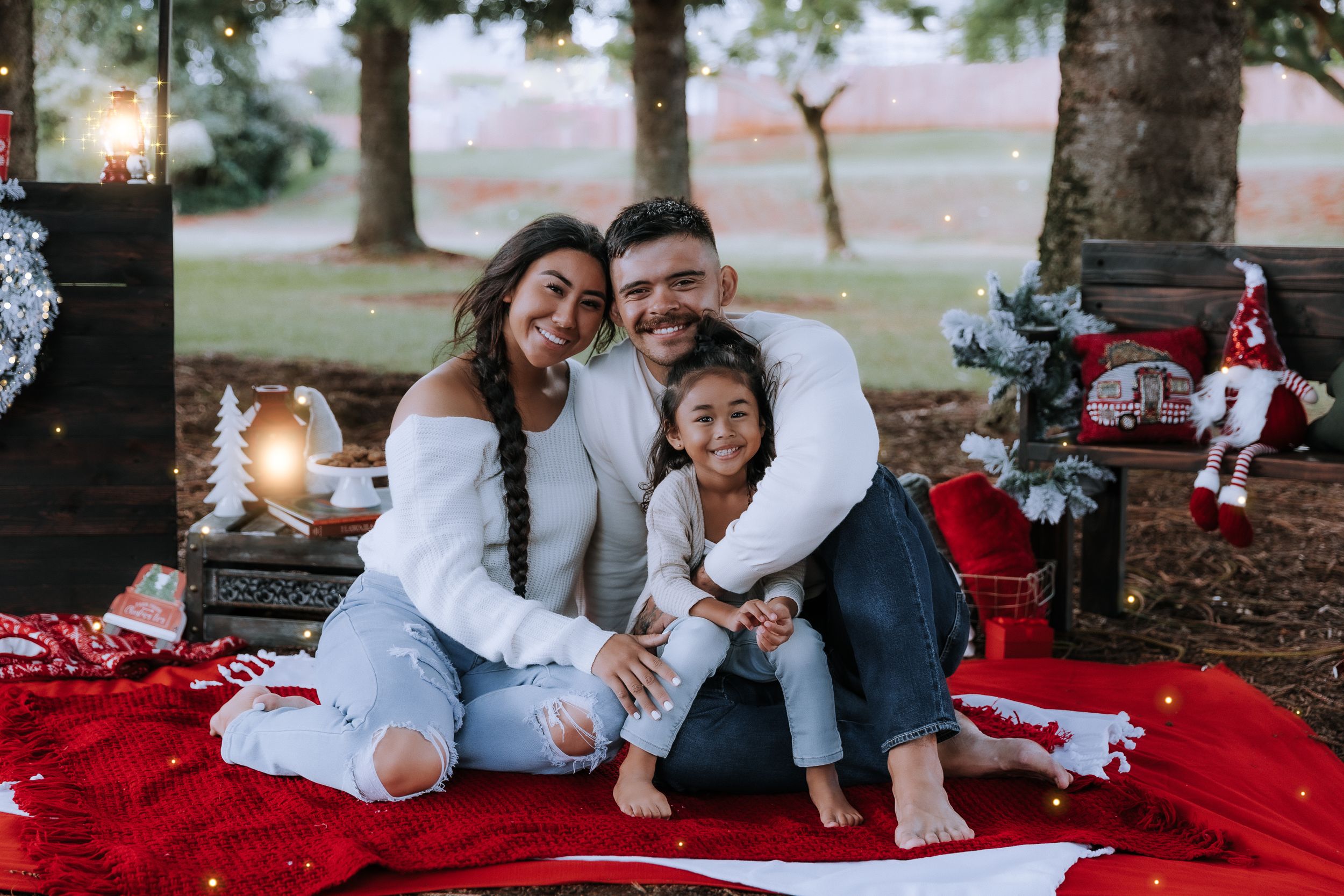 A family lounges together on a red blanket during an outdoor Christmas photo session.