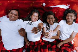 A family in white shirts and red plaid pants poses together for a holiday photo.