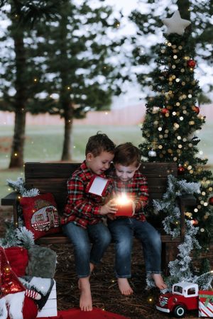 Children in matching plaid shirts sit on wooden benches surrounded by Christmas decorations and twinkling lights.