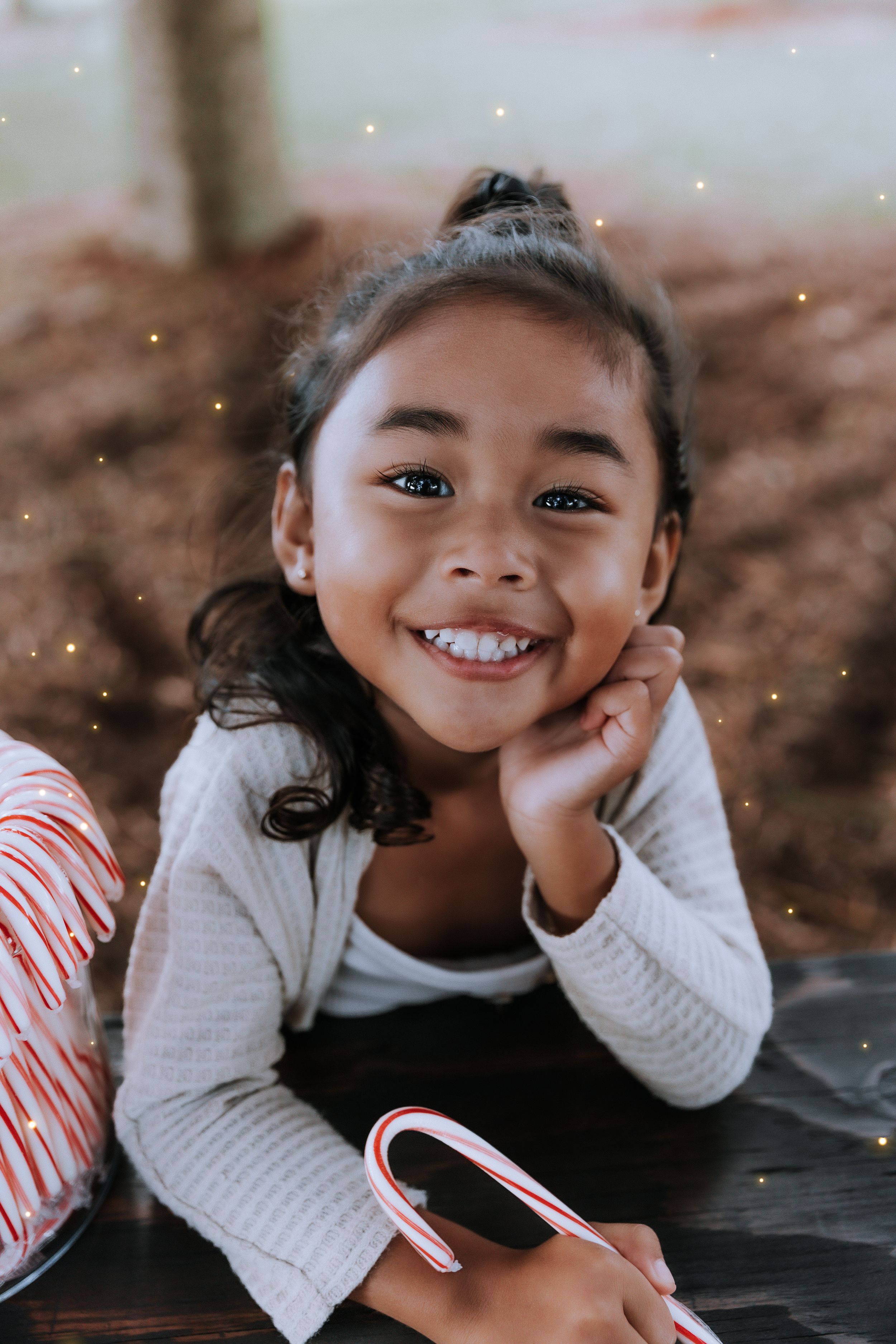 A child in a white sweater smiles joyfully during a holiday photoshoot.