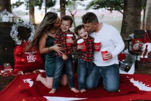 A family in matching plaid outfits sits together on a red blanket during Christmas.
