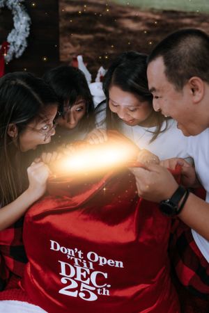 A family gathers around a red gift bag labeled 'Don't Open Until Dec 25' with magical light.