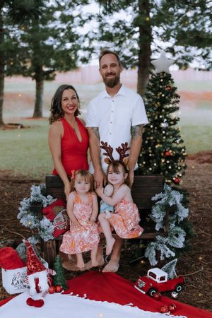 Christmas family portraits with decorated tree and holiday props on red blanket.