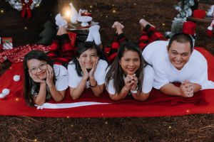 A family lies on a red blanket outdoors for a festive holiday photo.