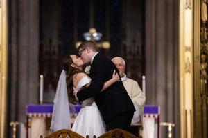Bride and groom share their first kiss at the altar with an officiant watching in a stunning cathedral.