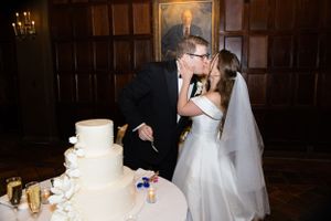 Newlyweds share a kiss while cutting their elegant white wedding cake at their reception.
