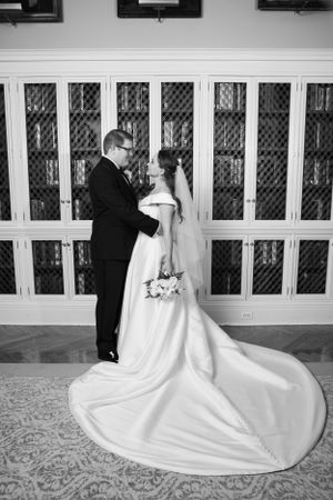 Black and white photo of bride and groom sharing intimate moment before ornate library cabinetry.