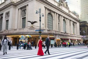 Engaged couple crosses a busy New York City street near Grand Central Terminal, woman in red gown.