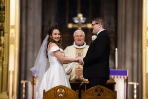 Bride and groom exchanging vows with elderly priest at ornate Gothic cathedral altar.