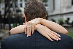 Close-up of a woman embracing her partner from behind, displaying a stunning diamond engagement ring.
