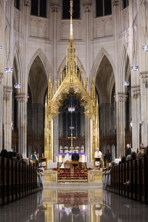 Grand Gothic cathedral interior with golden altar, soaring arches, and polished reflective marble floor.