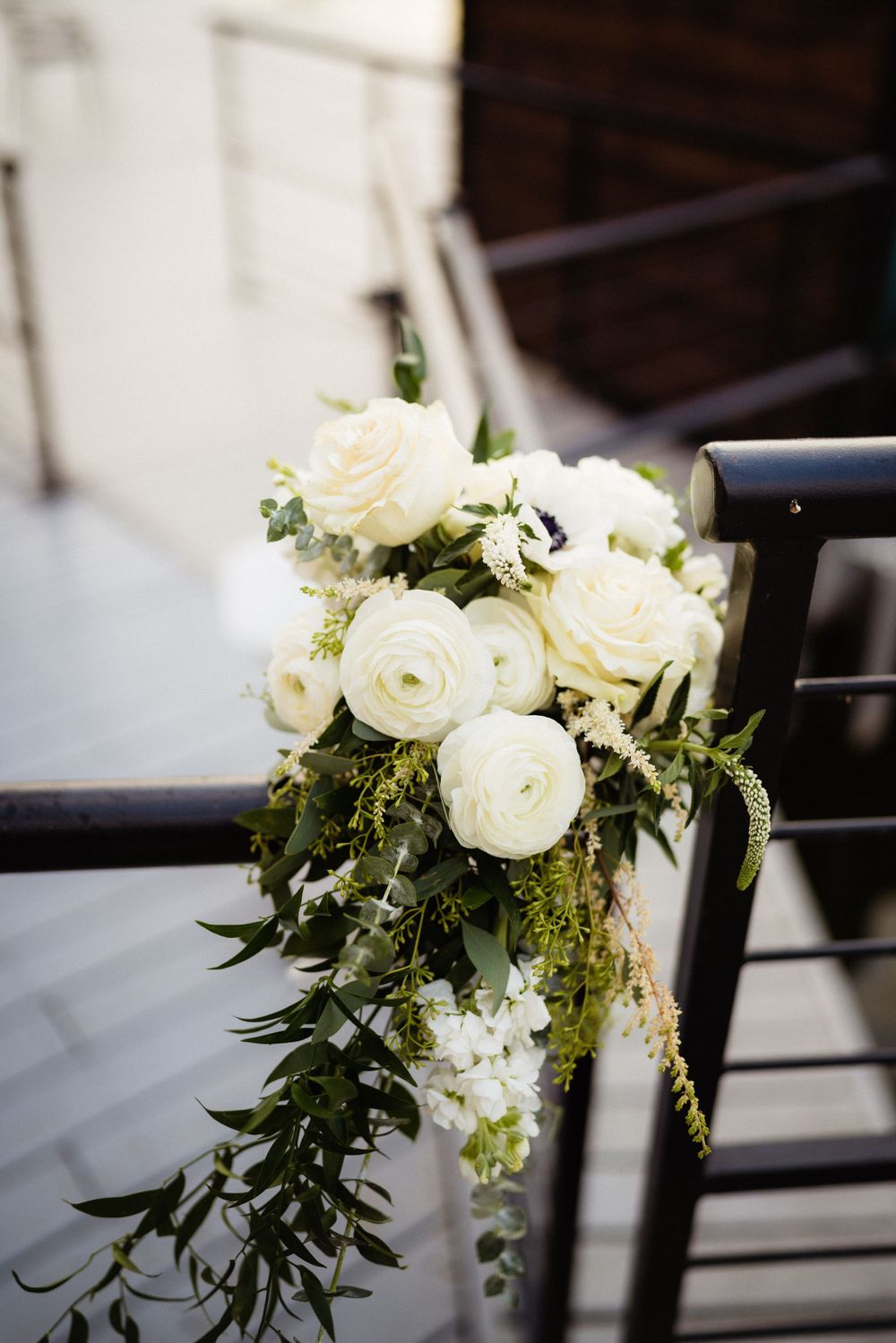 An elegant white rose and greenery floral arrangement decorates a dark metal railing.