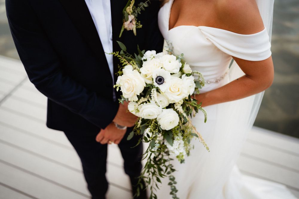 A close-up shot of a couple holding hands at a wedding ceremony with a white rose bouquet.