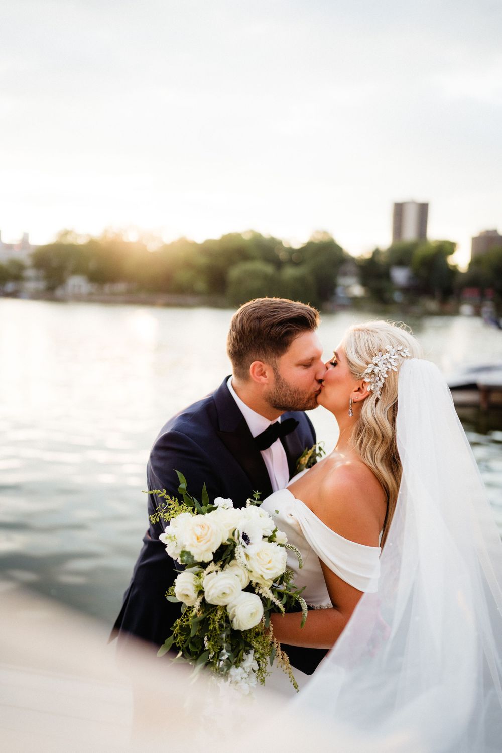 A tender wedding moment captured by the water with a white floral bouquet.