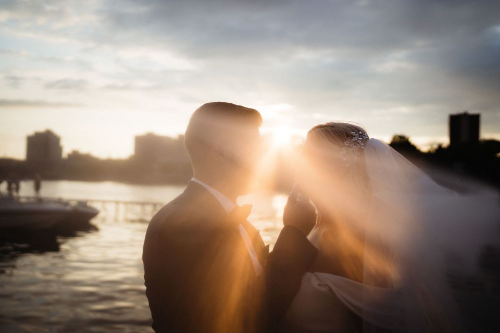 A silhouette of a couple during golden hour with sun flare and water in background.