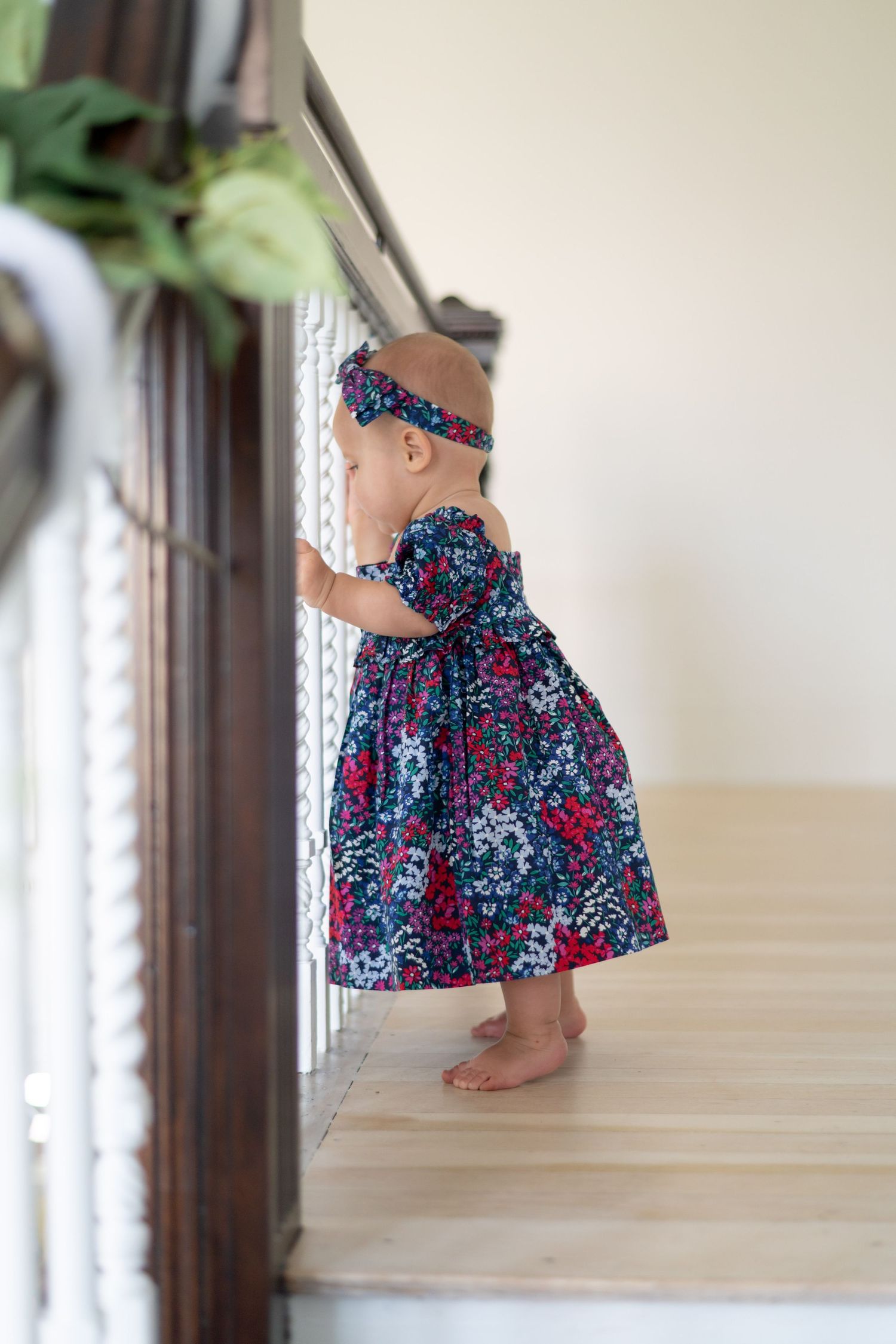 Little girl in a floral navy and red dress standing by a staircase.