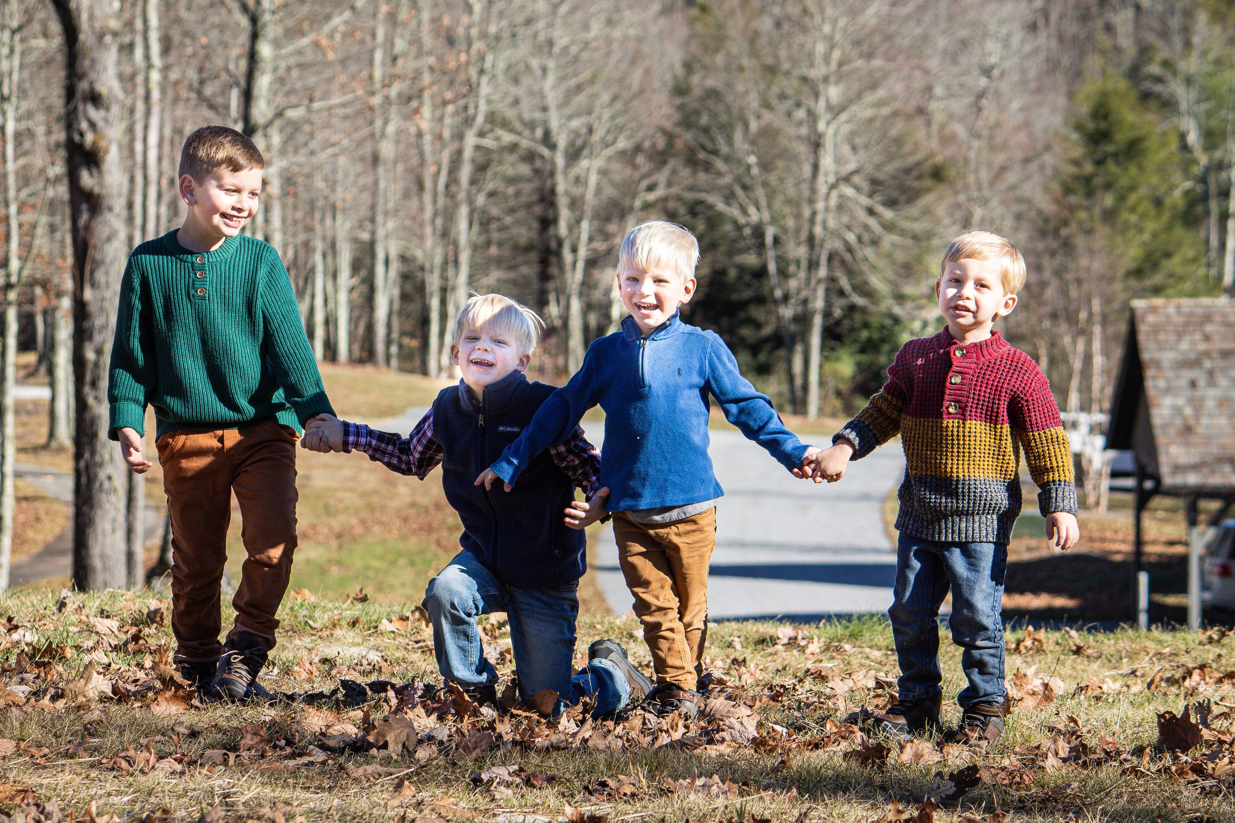 Four young children run and play together while holding hands outdoors in fall weather.