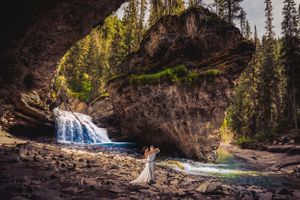 bride and groom stand in front of a waterfall