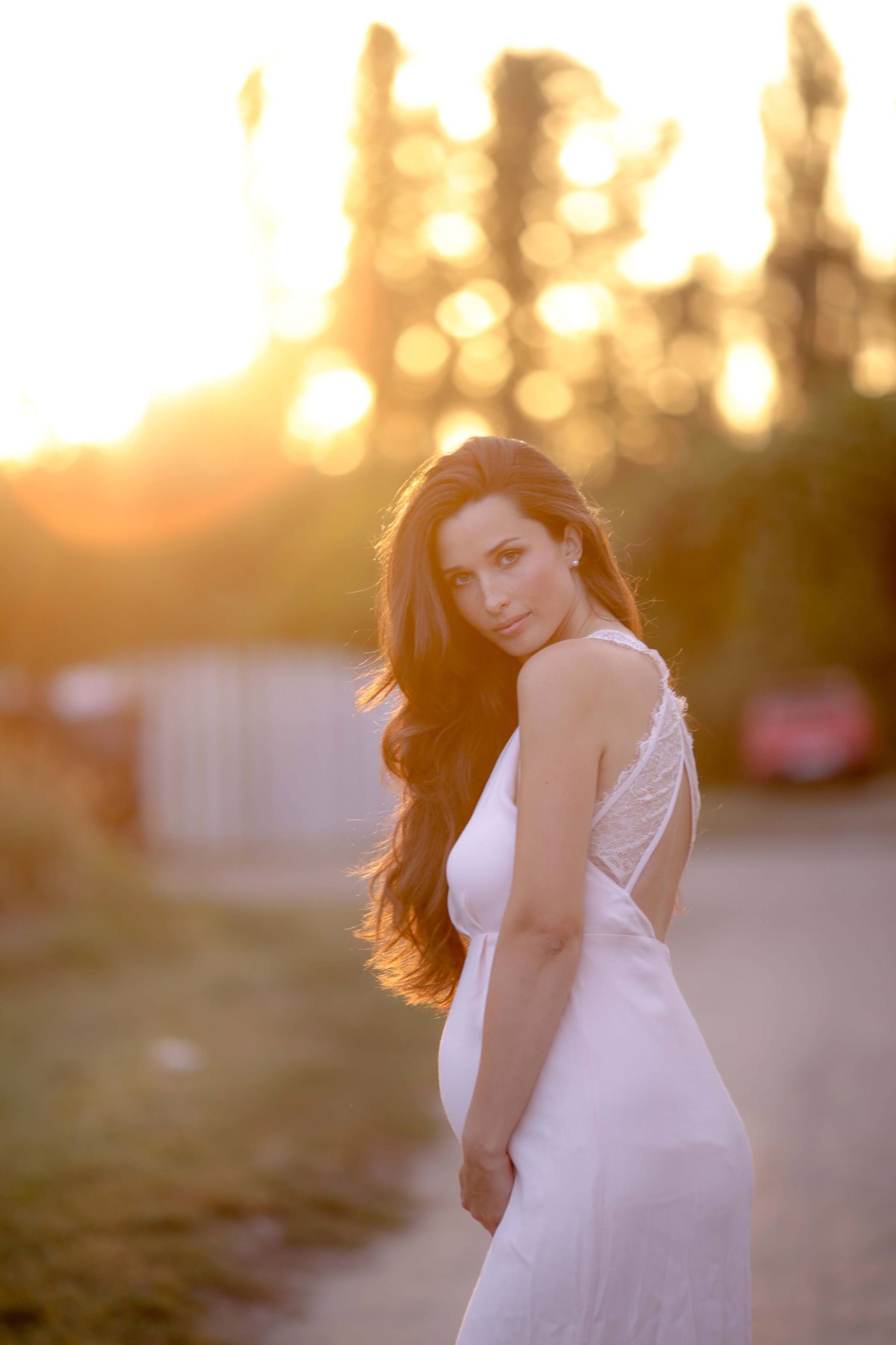 Sunset maternity portrait in form-fitting white dress showing silhouette.
