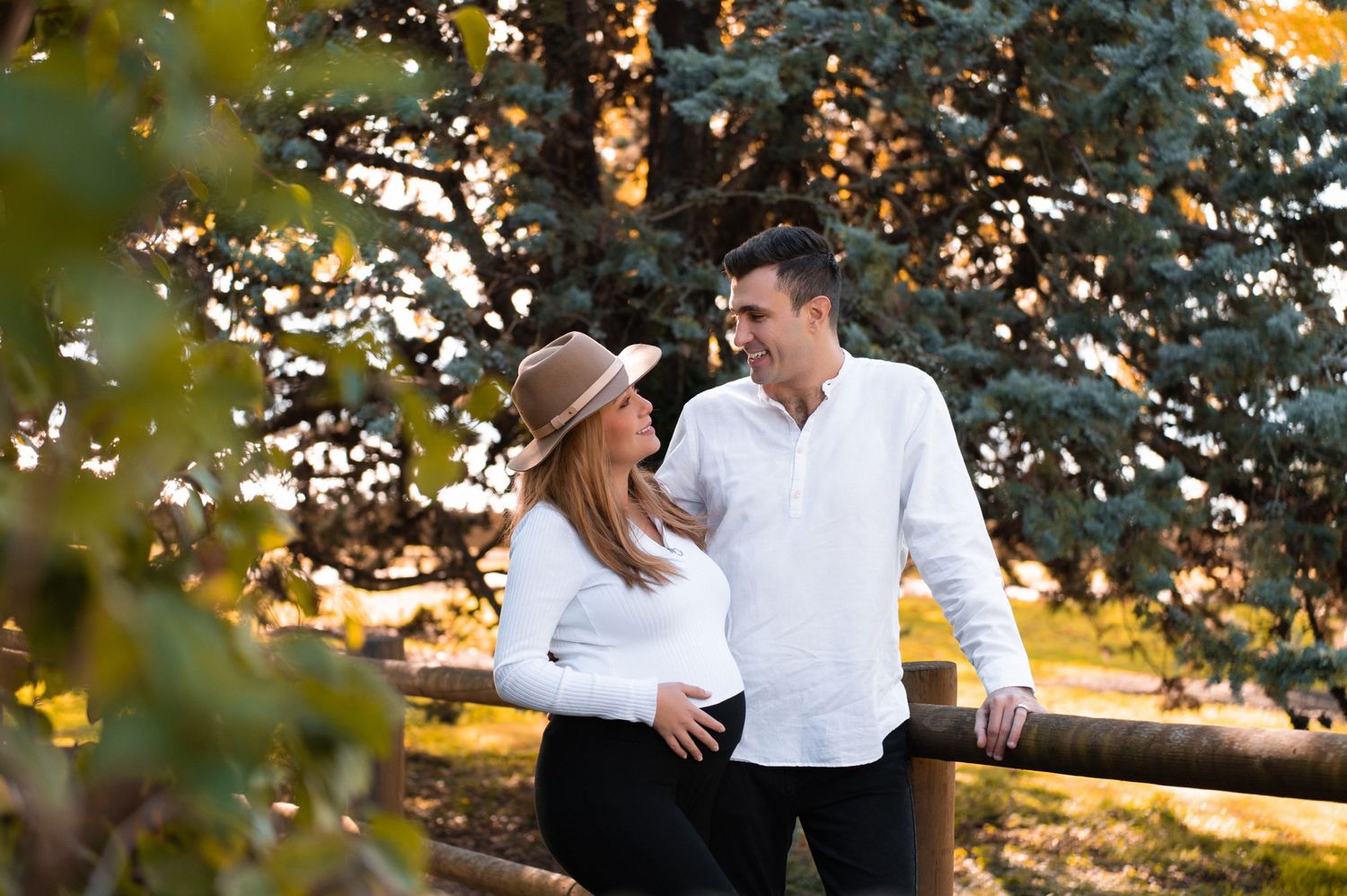 Couple shares a romantic moment under evergreen trees at sunset.