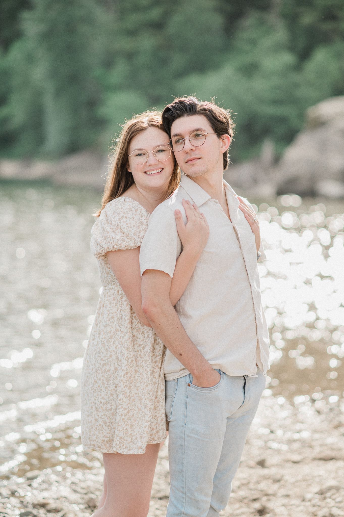 A couple poses together near a lake in casual summer attire during a romantic outdoor photo session.