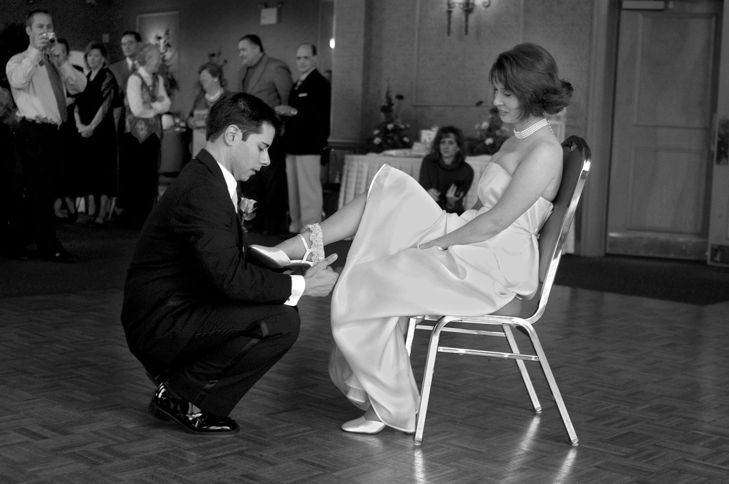 A traditional wedding garter removal ceremony taking place on a dance floor with guests watching.