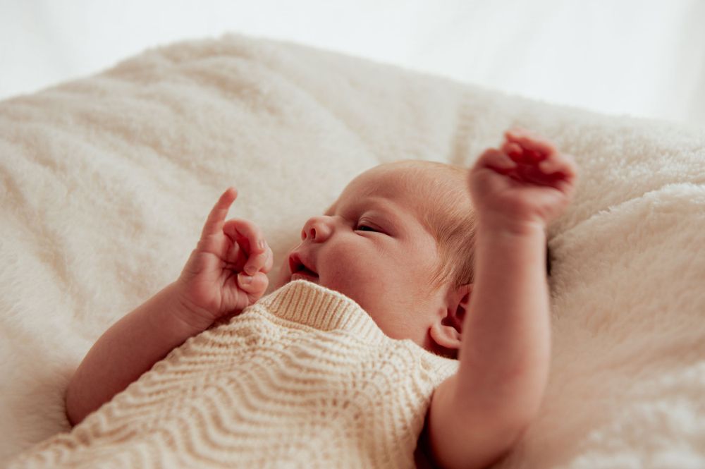 Baby in white knitted sweater stretches and yawns while lying on soft bedding.
Altona Family Photographer Melbourne