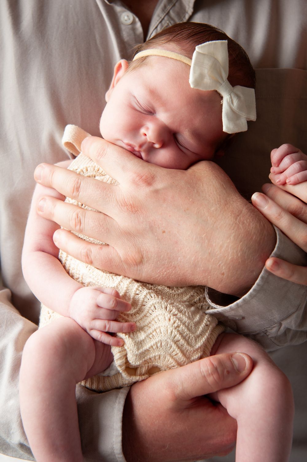 Sleeping infant in white bow and lace outfit cradled in gentle hands.
Altona Family Photographer Melbourne