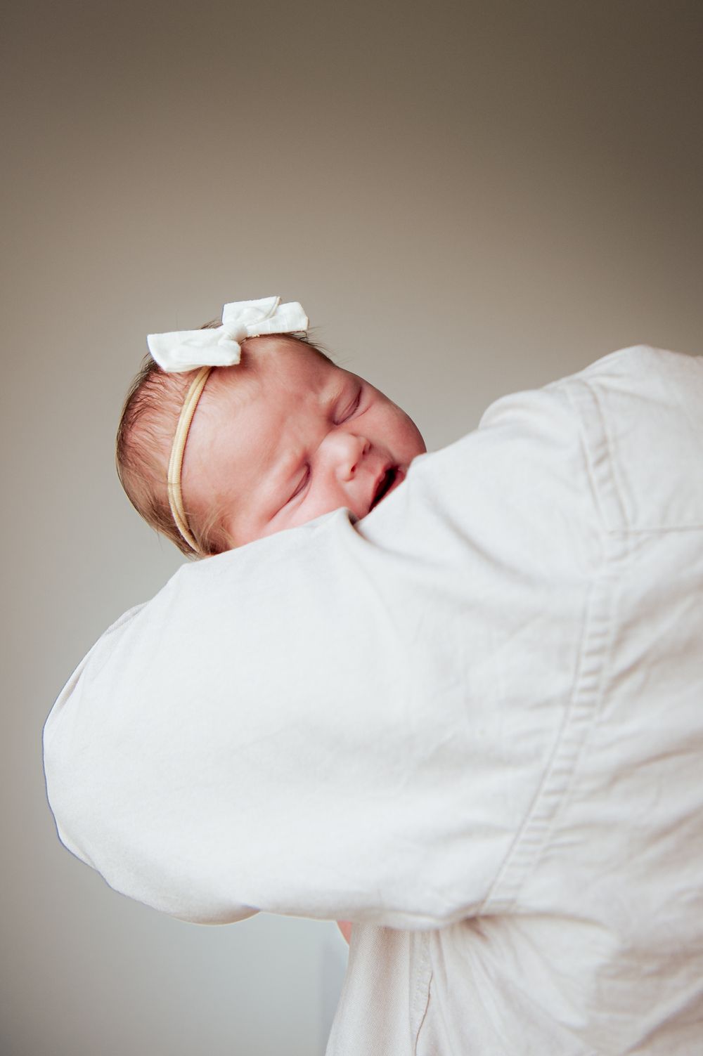 Sleeping newborn baby wearing white bow headband rests against soft white blanket.
Altona Family Photographer Melbourne