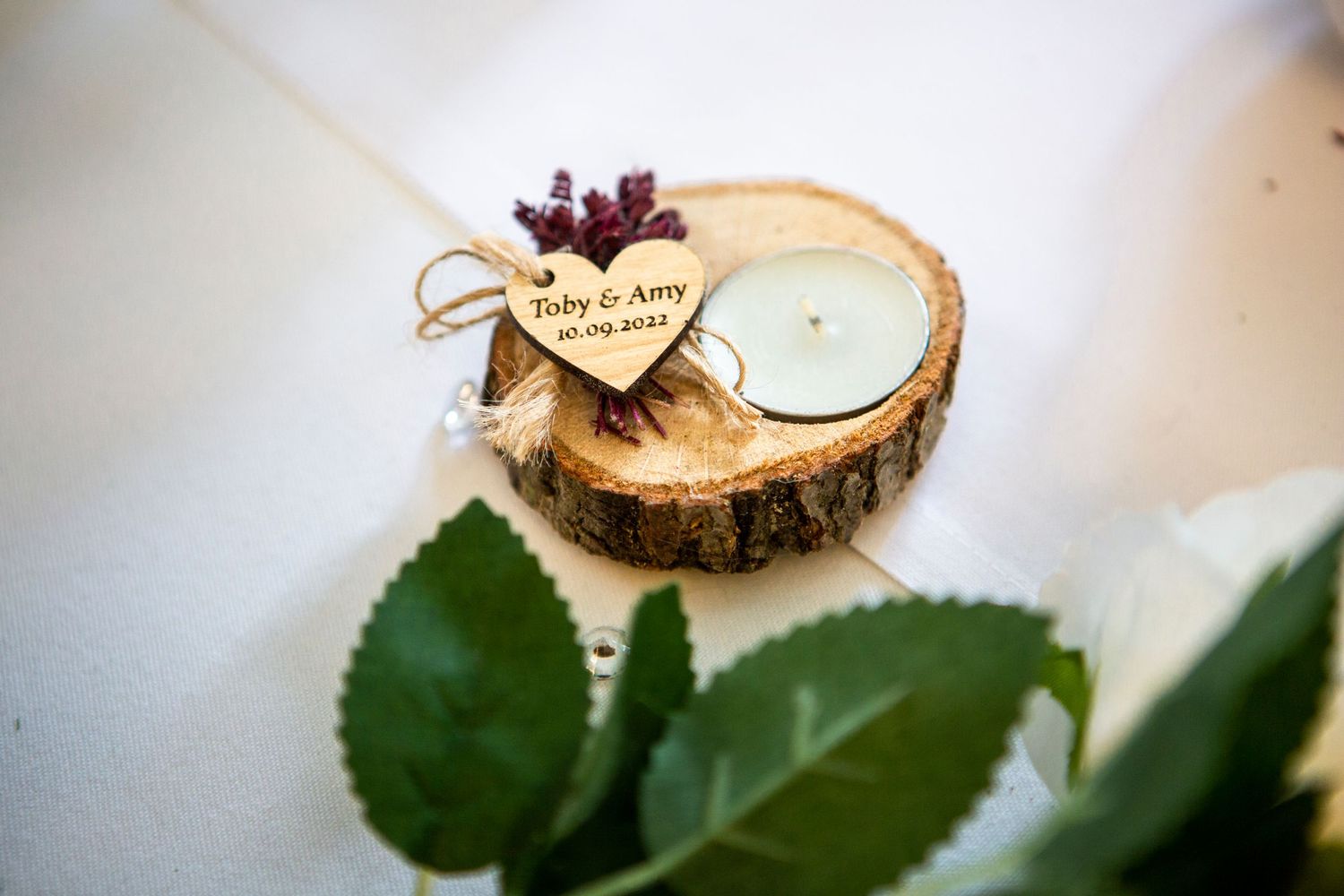 Rustic wooden slice wedding favor with heart tag engraved Toby and Amy, candle and greenery.