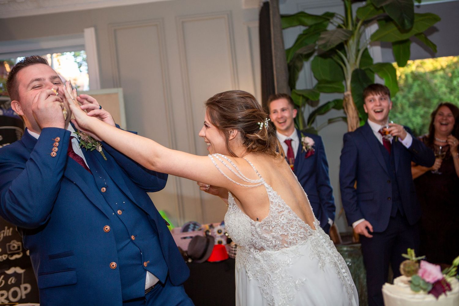 Bride playfully smashes cake into groom's face during fun wedding reception celebration.