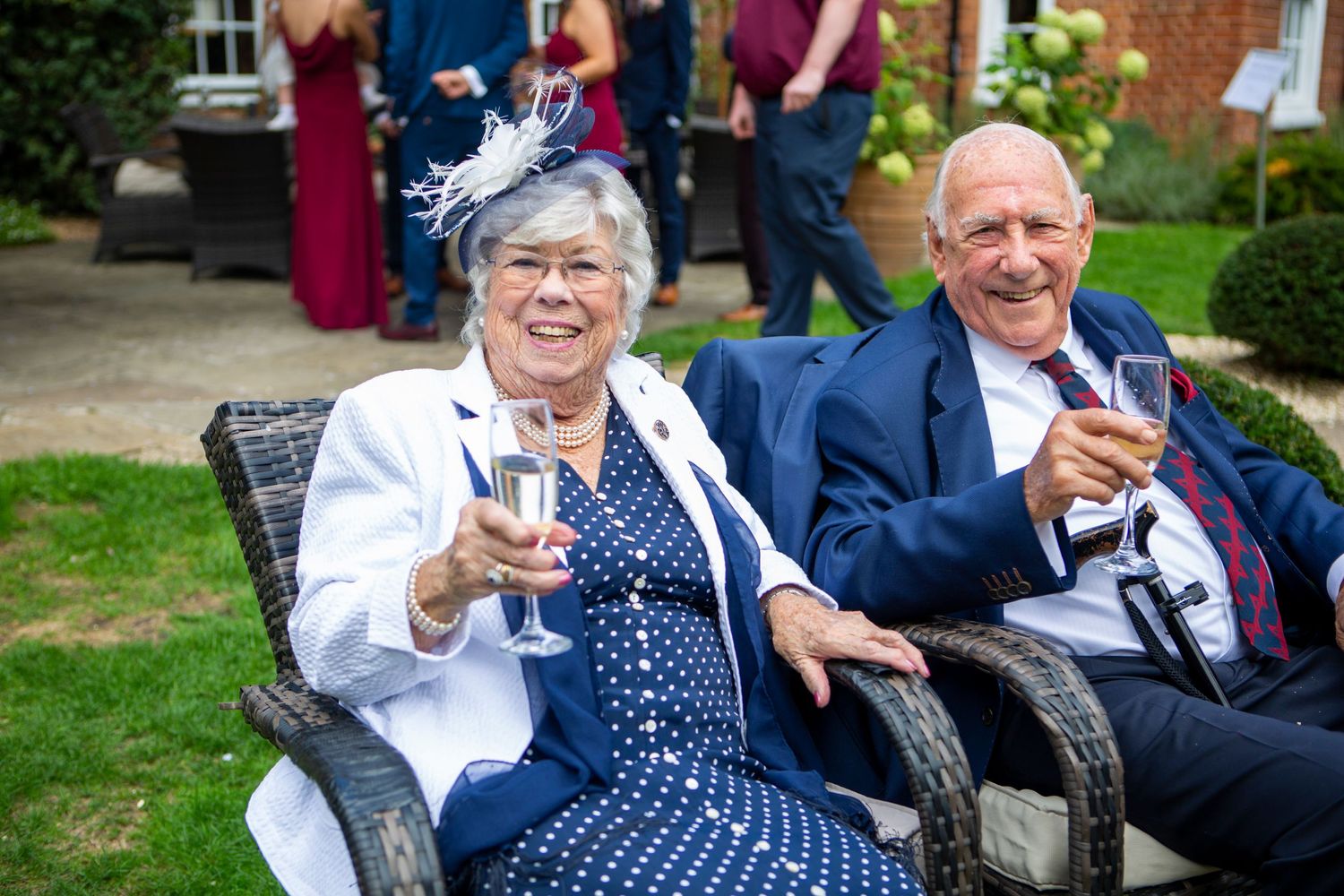 Elderly couple smiling and raising champagne glasses at an outdoor wedding reception celebration.