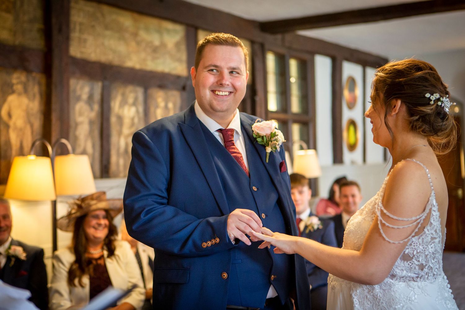 Groom smiles joyfully as bride places wedding ring on his finger during ceremony.
