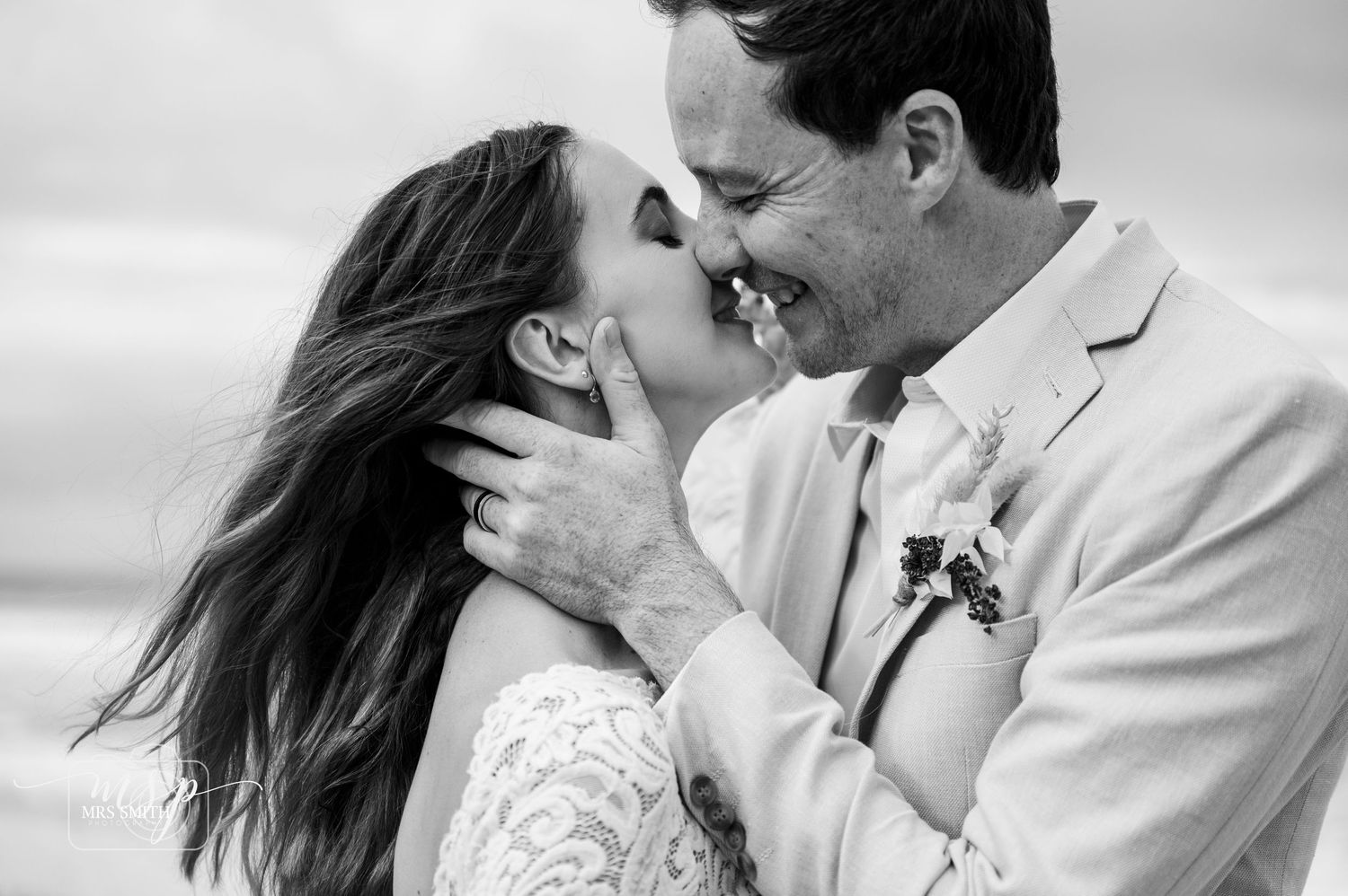 Black and white portrait captures an intimate moment between newlyweds against cloudy sky.