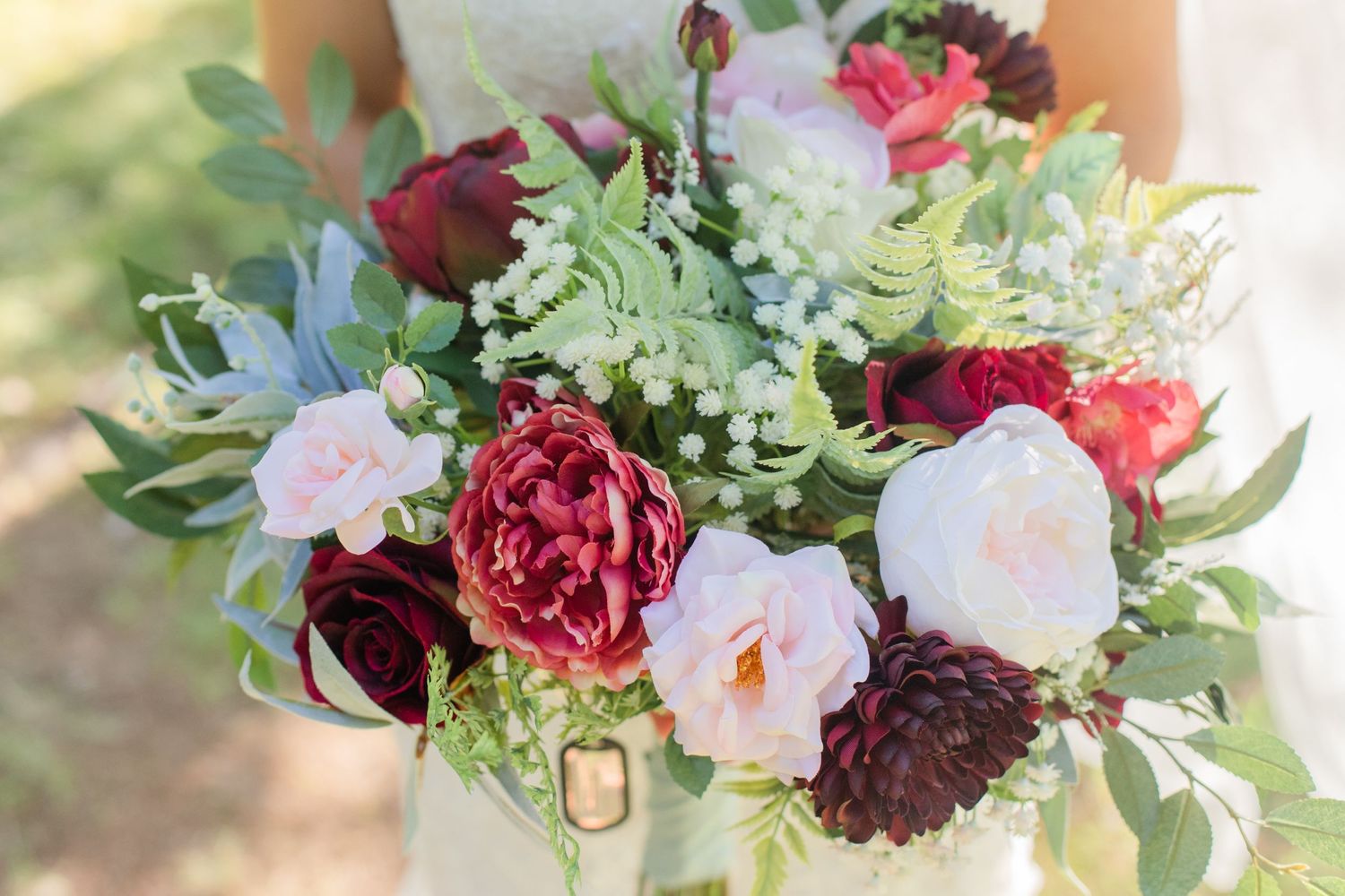 Close-up of romantic burgundy and pink wedding bouquet with mixed flowers and greenery.
