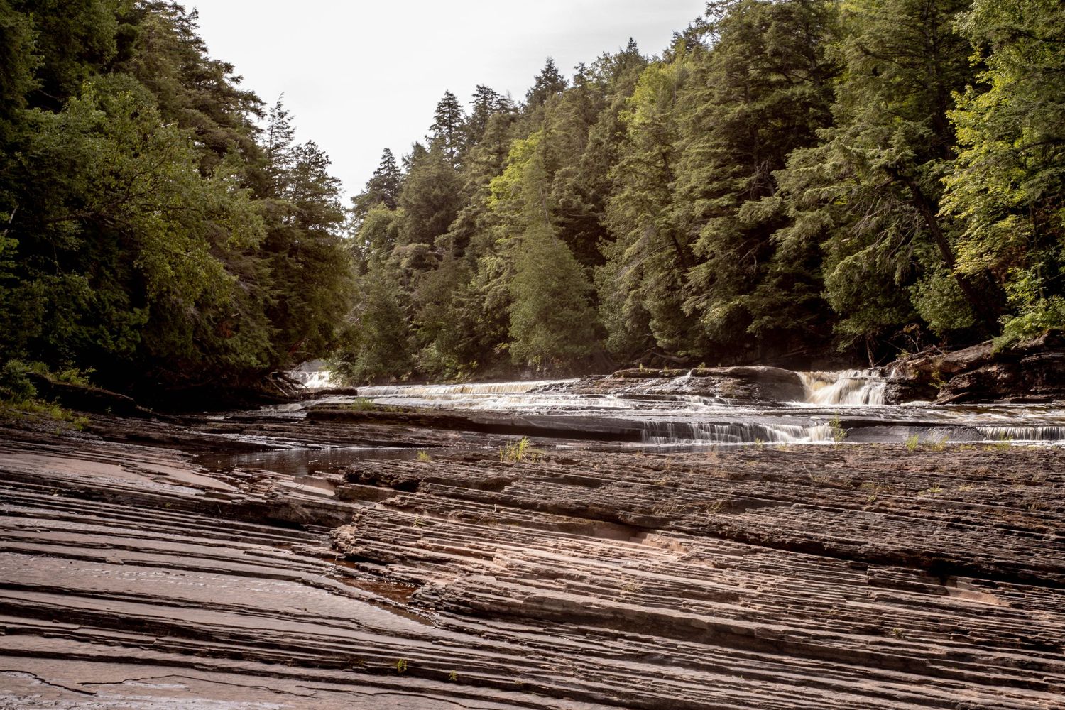 Cascading waterfall flowing over layered rock formations in a dense forest.