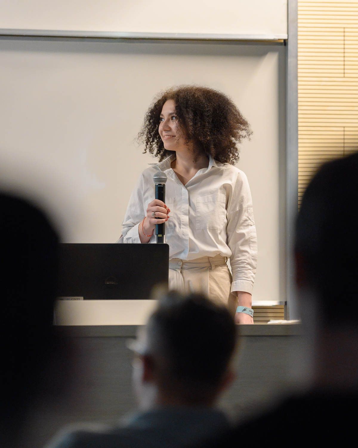 A speaker presents to an audience in a classroom setting with natural lighting.