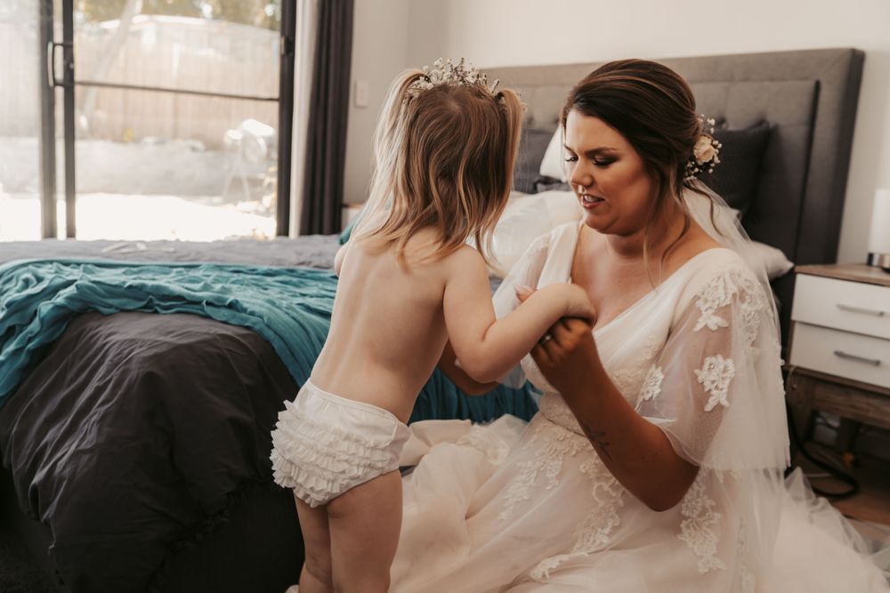 pregnant bride in blush lace dress helping young daughter get ready