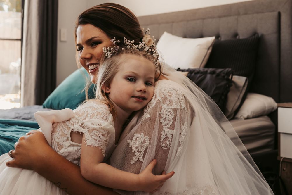 brunette bride in blush dress cuddling young daughter in white while smiling
