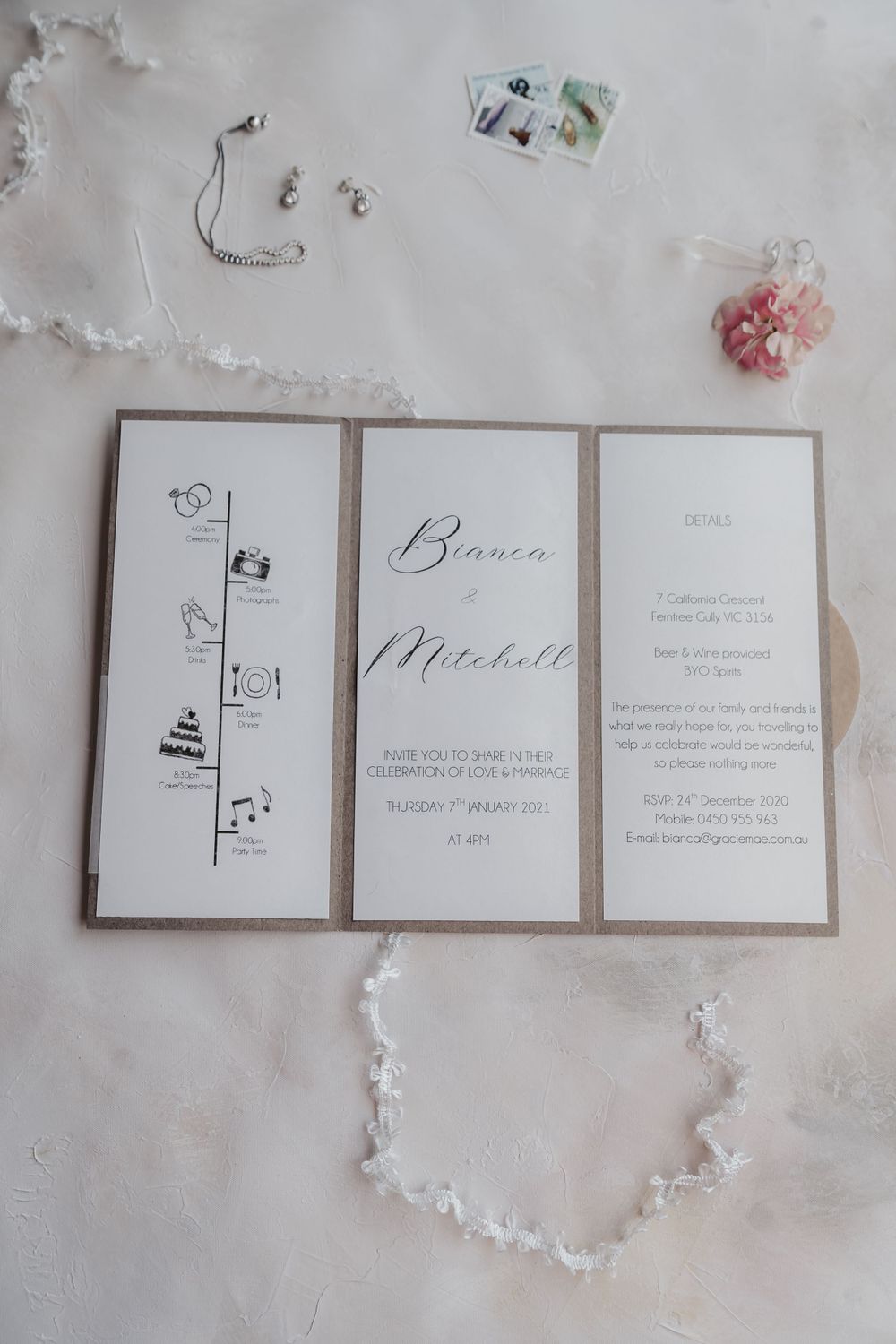 flatlay of invitation in white and gold on blush background with pink and white accessories