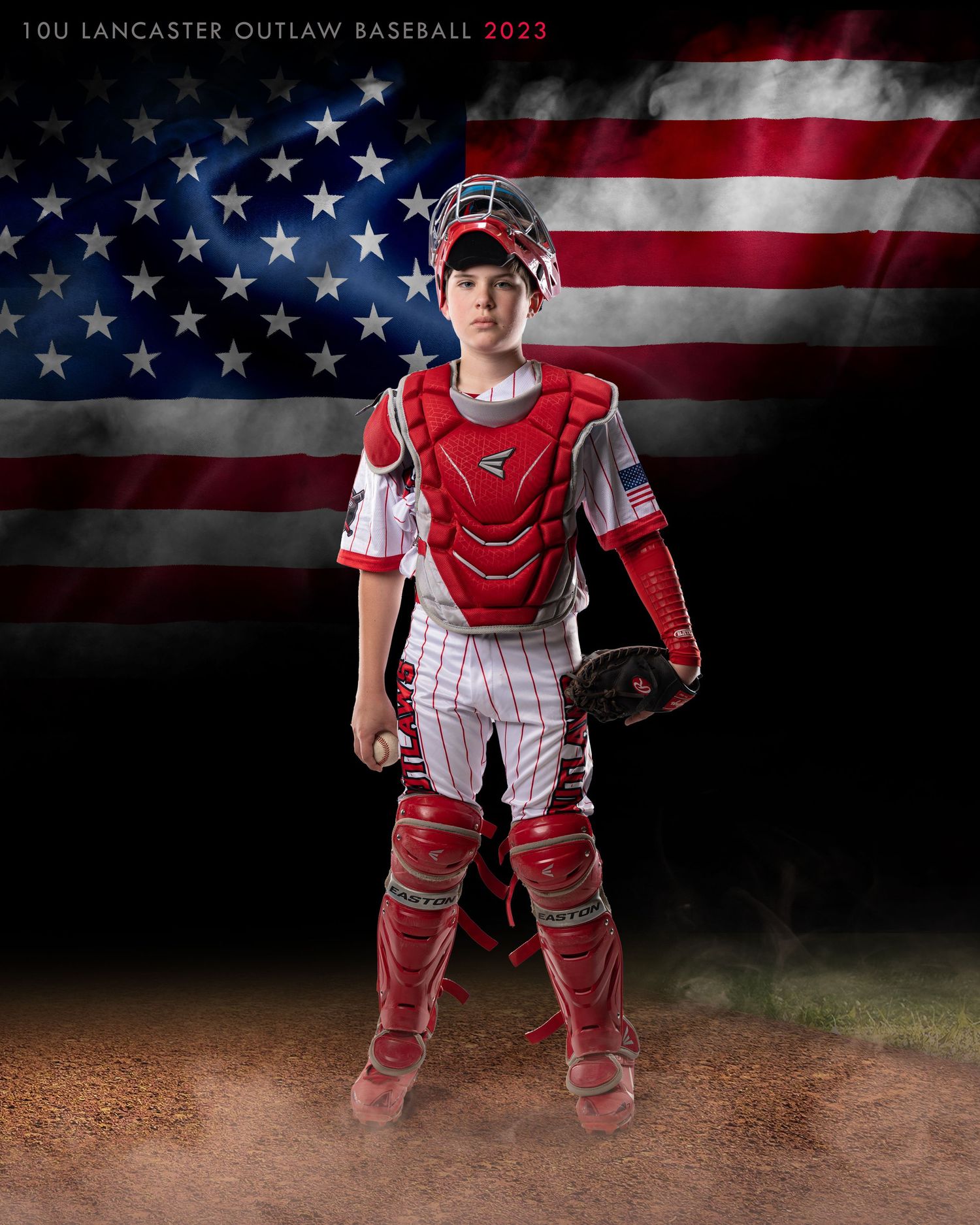 Youth baseball catcher in red gear poses dramatically against American flag backdrop.