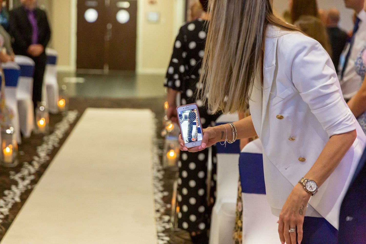 Wedding guest holds her phone out to video the bride as she walks down the aisle. Crowne Plaza Hotel Liverpool.