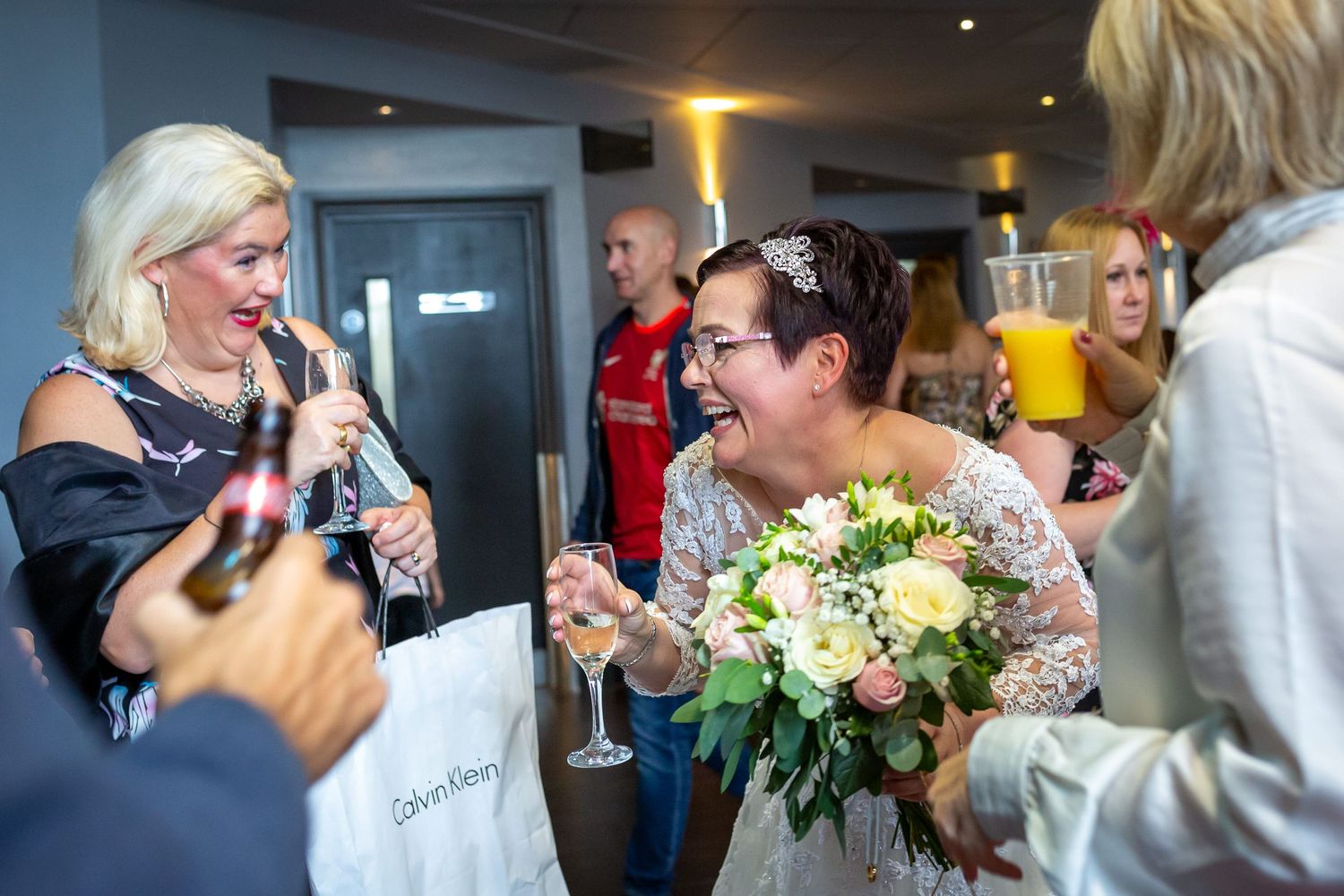 Bride after the ceremony laughing with her friends holding a glass of champagne at the Crowne Plaza Hotel Liverpool