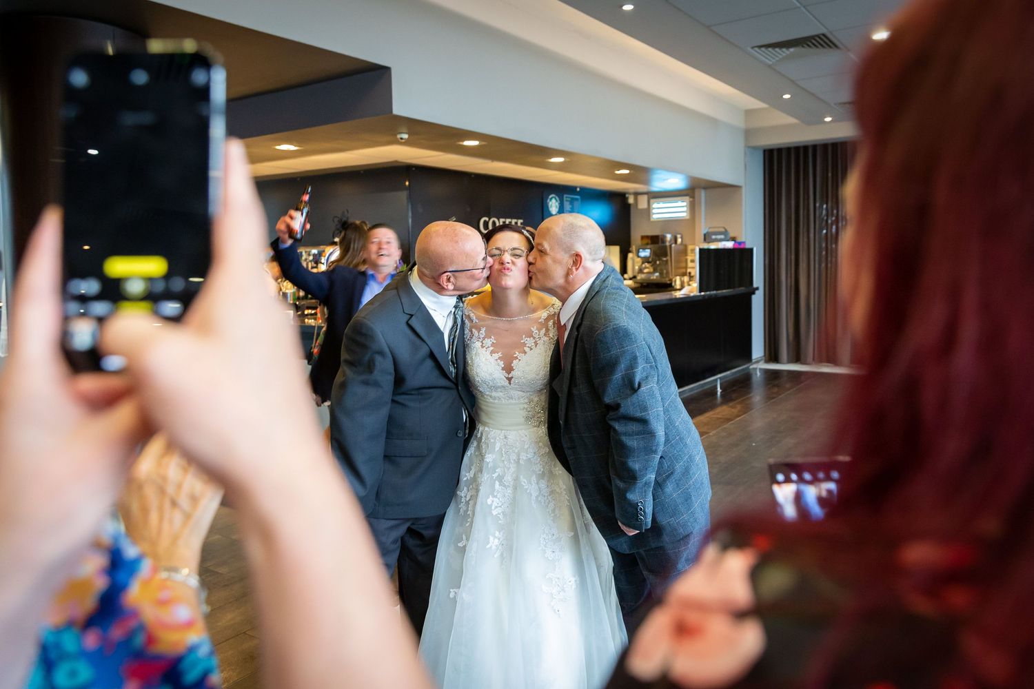 Bride gets a kiss on each cheek from a couple of male guests in the bar at the Liverpool Crowne Plaza hotel