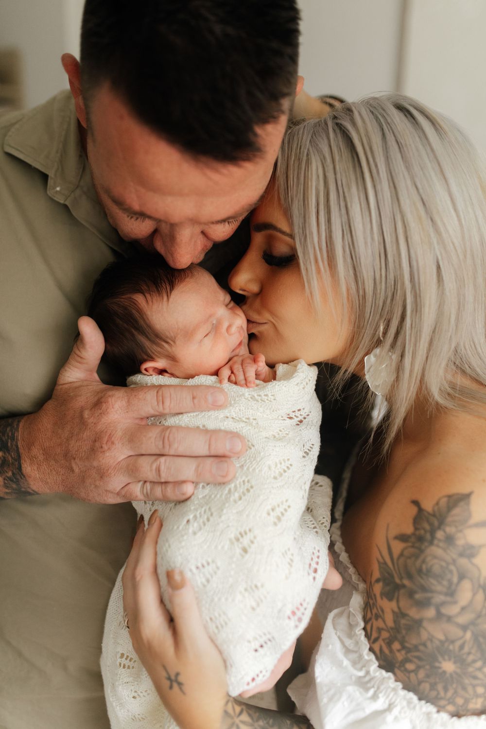 Parents sharing tender moment with newborn wrapped in white knit blanket.