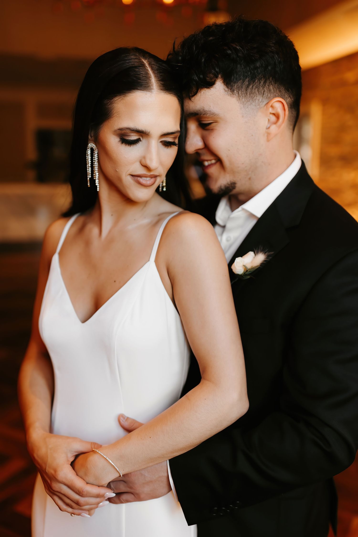 Intimate portrait of bride and groom embracing tenderly in warm golden light during wedding reception.