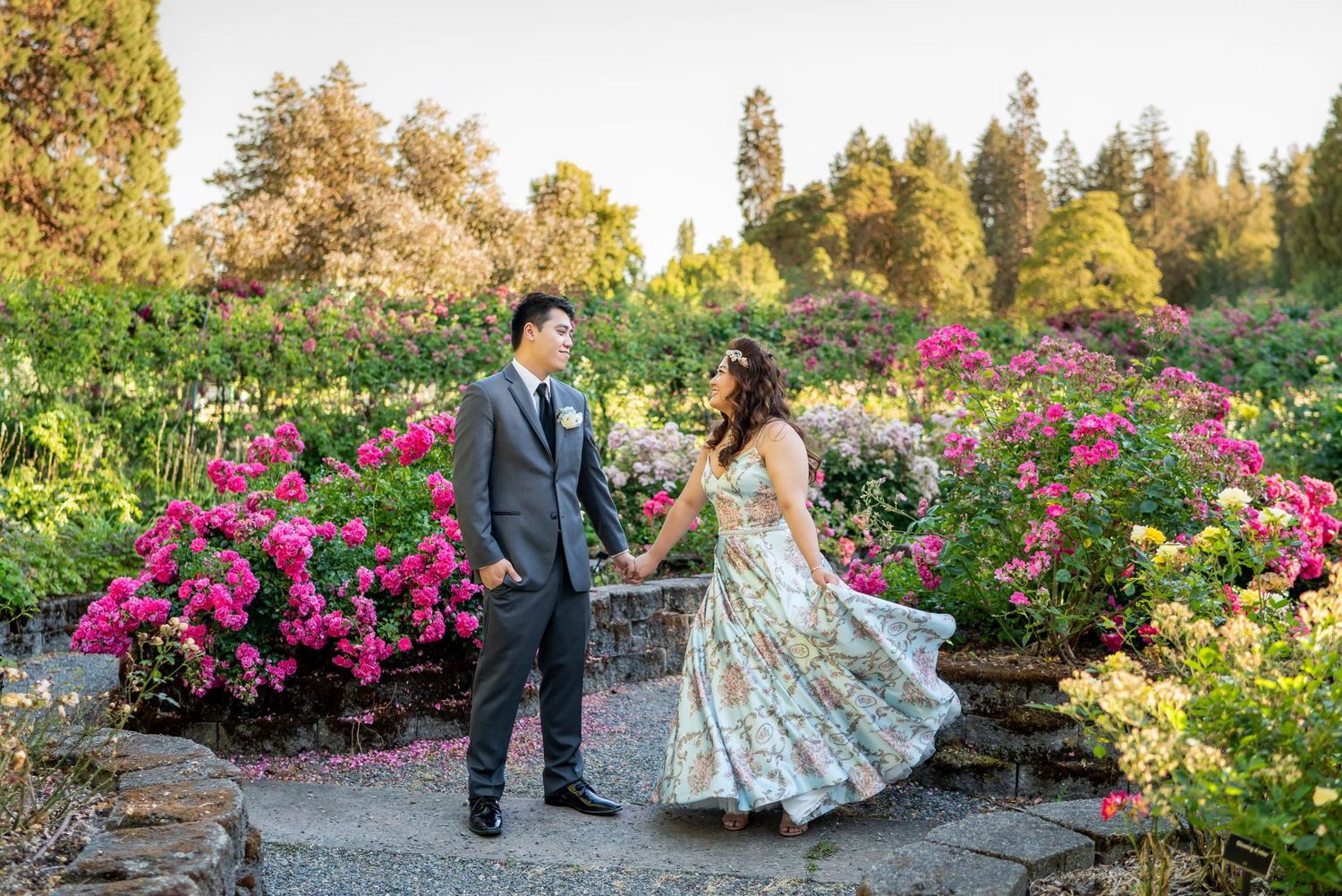 Wedding couple walking through vibrant garden with pink blooming flowers.