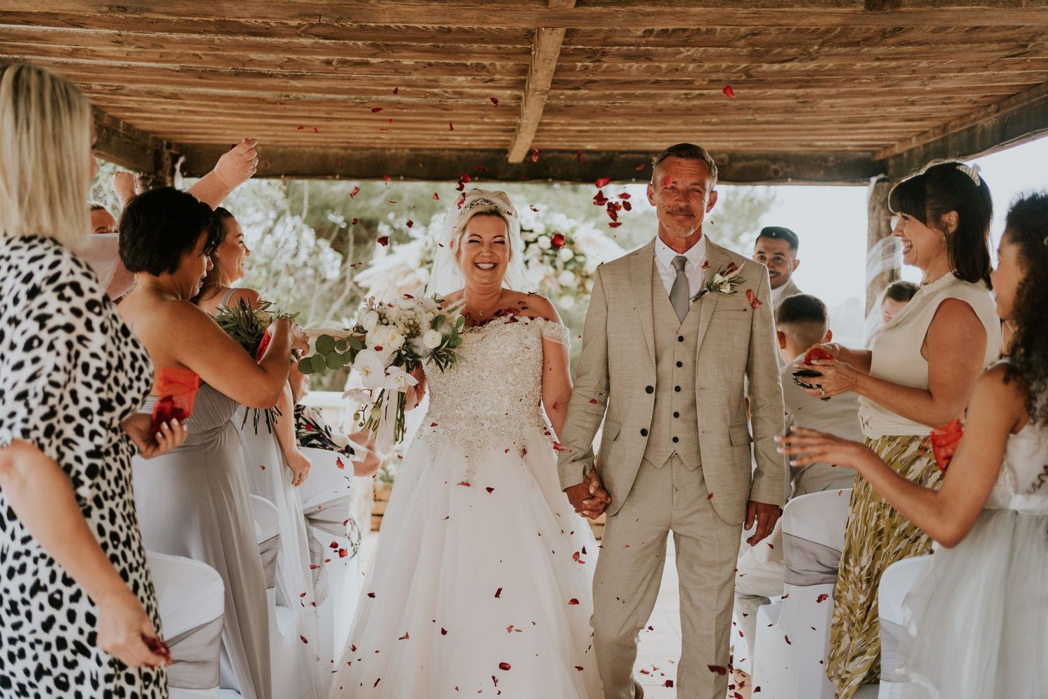 Outdoor wedding ceremony under a rustic wooden pergola with flower petals.