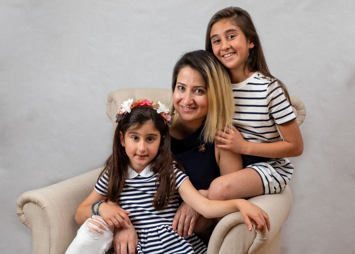 A loving family portrait of three in coordinated striped outfits sitting on a beige armchair.